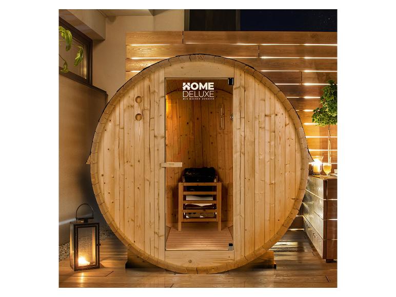 Home Deluxe Fasssauna auf einer Terrasse bei Nacht, mit Laterne und Pflanzen