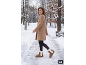 Frau in einem eleganten braunen Mantel und warmen Stiefeln auf einem verschneiten Weg.
