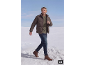 Mann in brauner Daunenjacke, grünem Pullover und Jeans, der durch den Schnee geht.