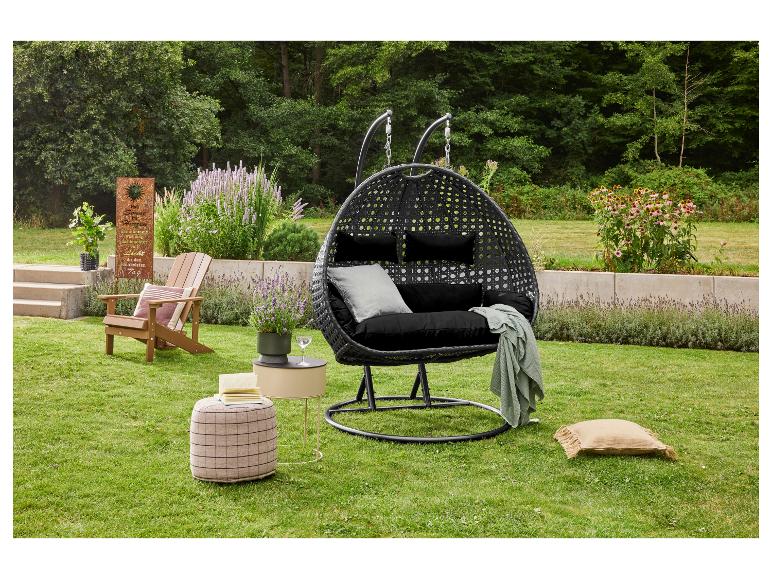 Schwarzer Hängesessel mit Kissen, Beistelltisch, Pouf und Gartenstuhl in einem grünen Garten.