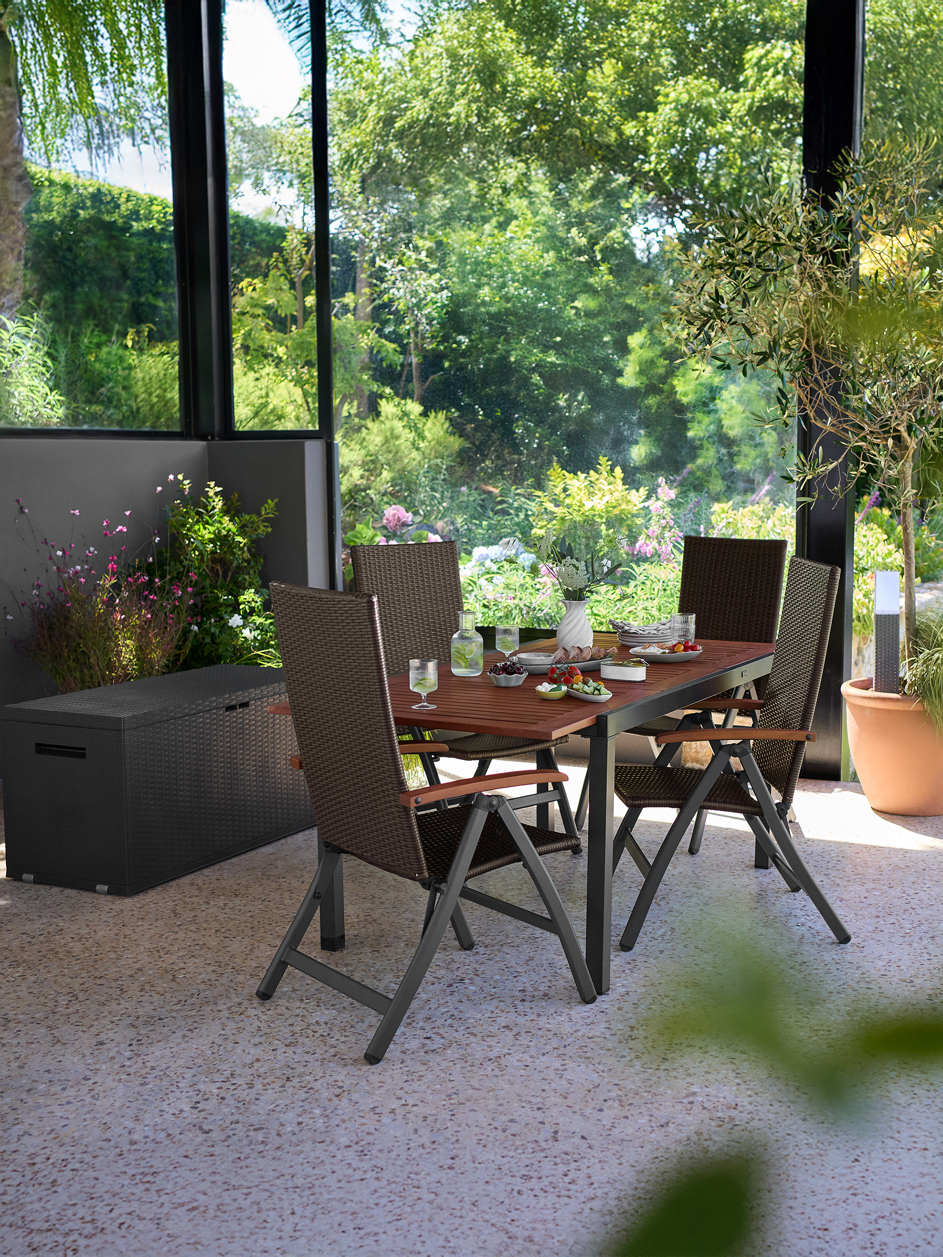 Terrassen-Essgruppe mit braunen Stühlen und Holztisch, umgeben von viel Grün.