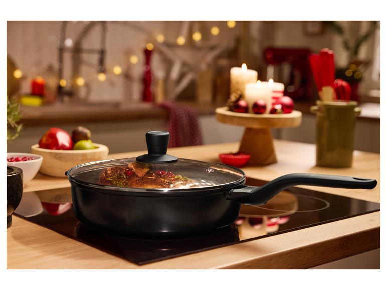 Schwarze Bratpfanne mit Glasdeckel auf einem Kochfeld, mit festlicher Dekoration im Hintergrund.