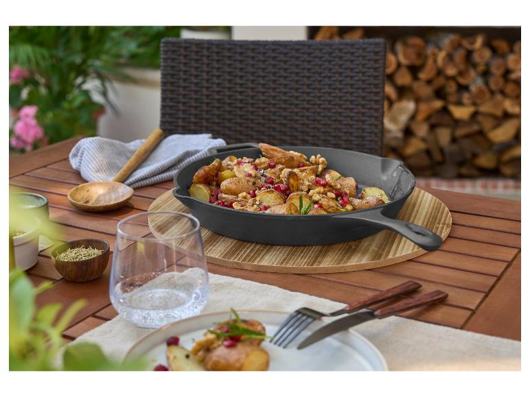 Gusseisenpfanne mit Kartoffeln, Granatapfel und Walnüssen auf einem Holztisch im Freien.