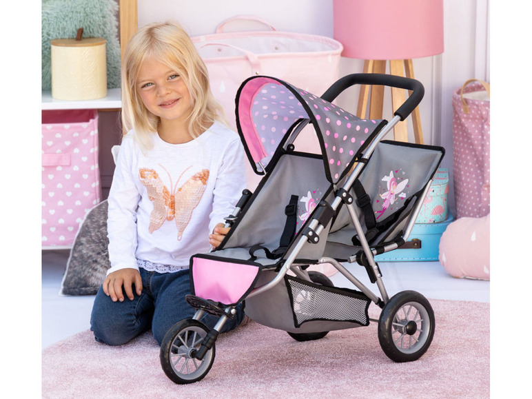 Ein Mädchen mit einem rosafarbenen Puppenwagen mit einem Schmetterlingsmotiv.