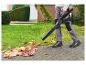 Person mit Laubbläser entfernt Blätter von einem gepflasterten Weg.