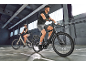 Zwei Personen fahren E-Bikes in einer Halle.