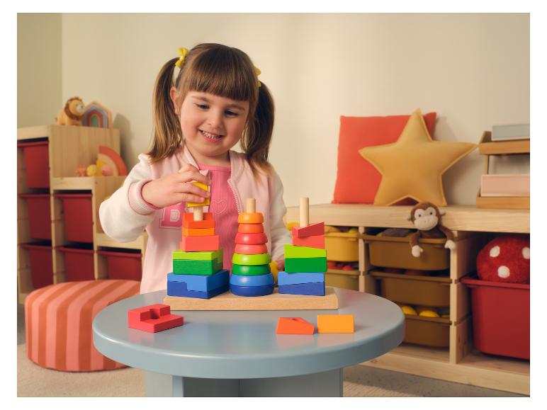Lächelndes Mädchen spielt mit bunten Holz-Stapelspielzeugen auf einem grauen Tisch im Spielzimmer.