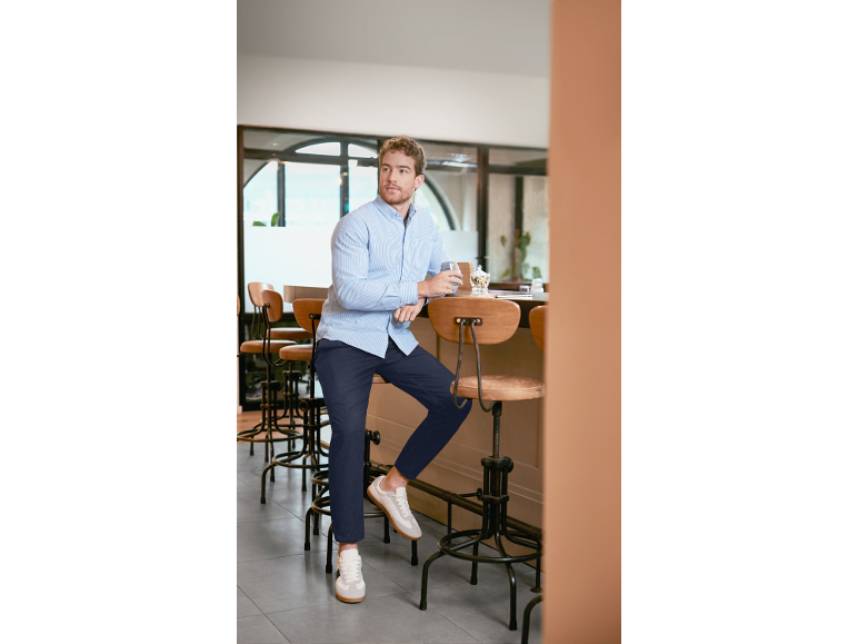 Mann in blauem Hemd und dunkelblauer Hose sitzt an einer Bar.