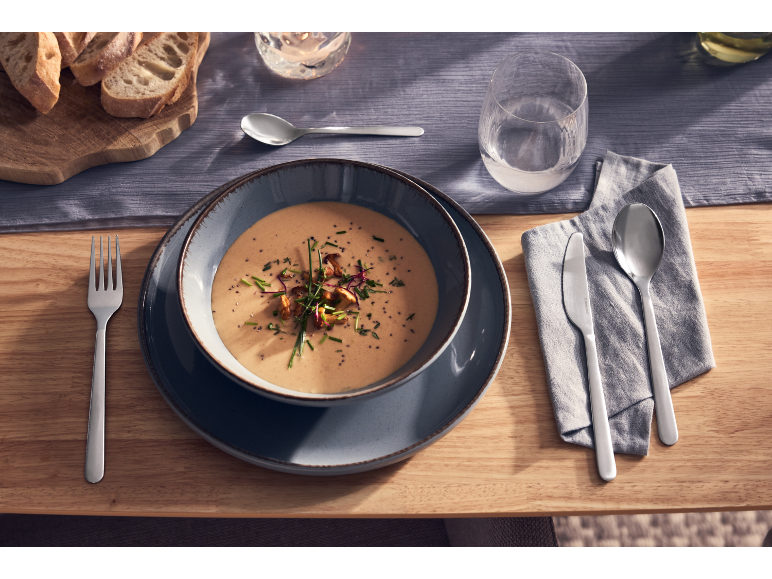 Eine Schüssel cremige Suppe serviert mit Besteck und Brot auf einem gedeckten Tisch.