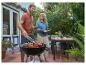 Mann grillt Steaks und Tomaten, Frau bringt Brot draußen im Garten.