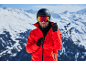 Mann mit Skihelm, Skibrille und roter Jacke in verschneiten Bergen.