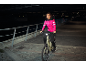 Frau in pinker Jacke und schwarzer Hose auf E-Bike bei Nacht