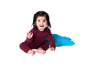 Fröhliches Baby in bordeauxrotem Strickanzug sitzt neben einem blauen Kissen.