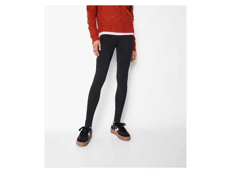 Schwarze Damenleggings mit orangefarbenem Pullover und schwarzen Sneakern.