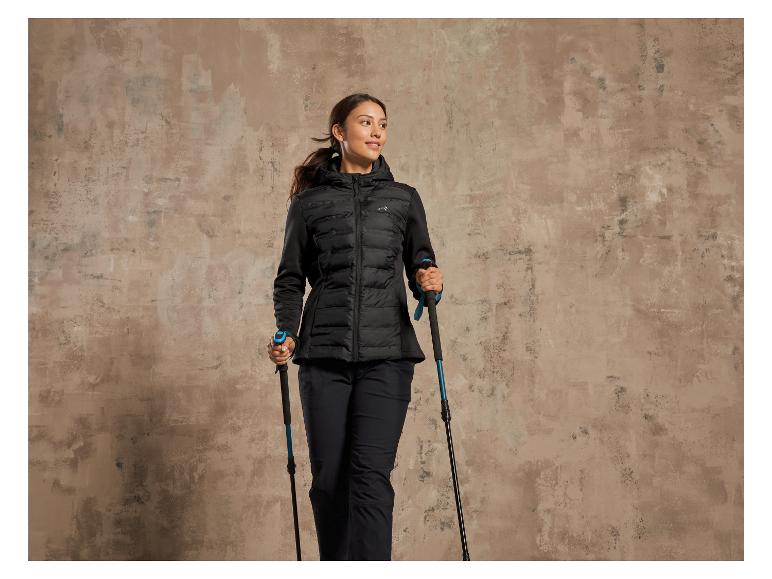 Eine Frau in einer schwarzen Winterjacke und Wanderstöcken.