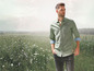 Mann in grünem Hemd und Jeans steht auf einem Feld mit Blumen.