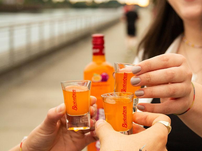 Drei Personen stoßen mit Berentzen-Shots an, eine Flasche im Hintergrund.