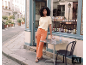 Frau in gelbem Strick-T-Shirt und orangefarbener Wide-Leg-Hose vor einem Geschäft.