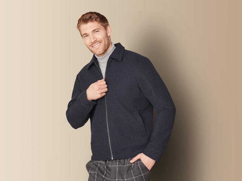 Ein Mann trägt eine dunkelblaue Jacke mit Reißverschluss und eine karierte Hose.