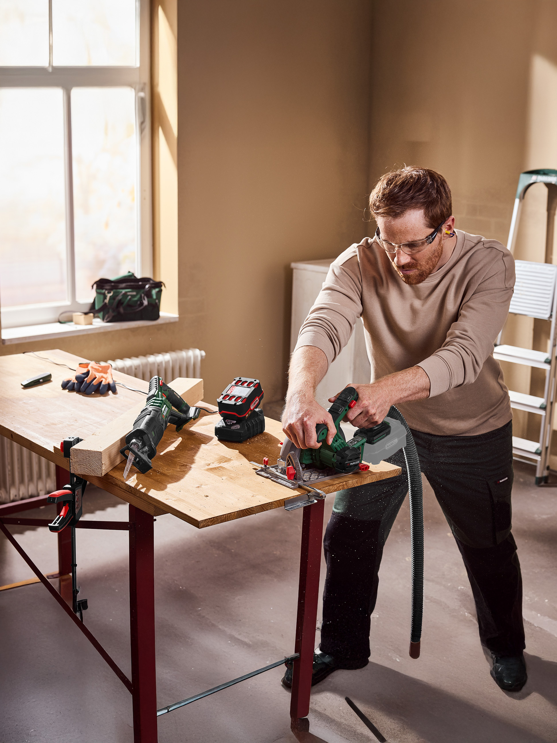 Ein Mann benutzt eine Kreissäge, um Holz auf einer Werkbank zu schneiden, mit einer Säbelsäge in der Nähe.