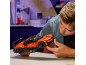 Ein junger Mann baut an einem Tisch ein orangefarbenes Spielzeug-Sportauto zusammen.