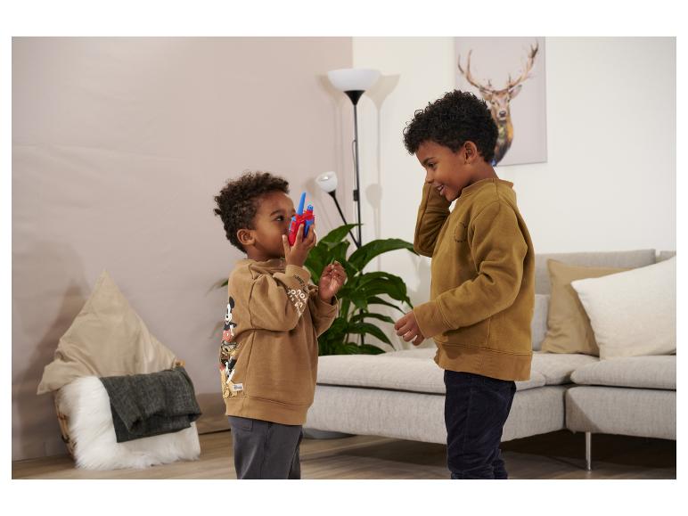 Zwei Jungen in braunen Sweatshirts spielen mit einem Walkie-Talkie im Wohnzimmer.