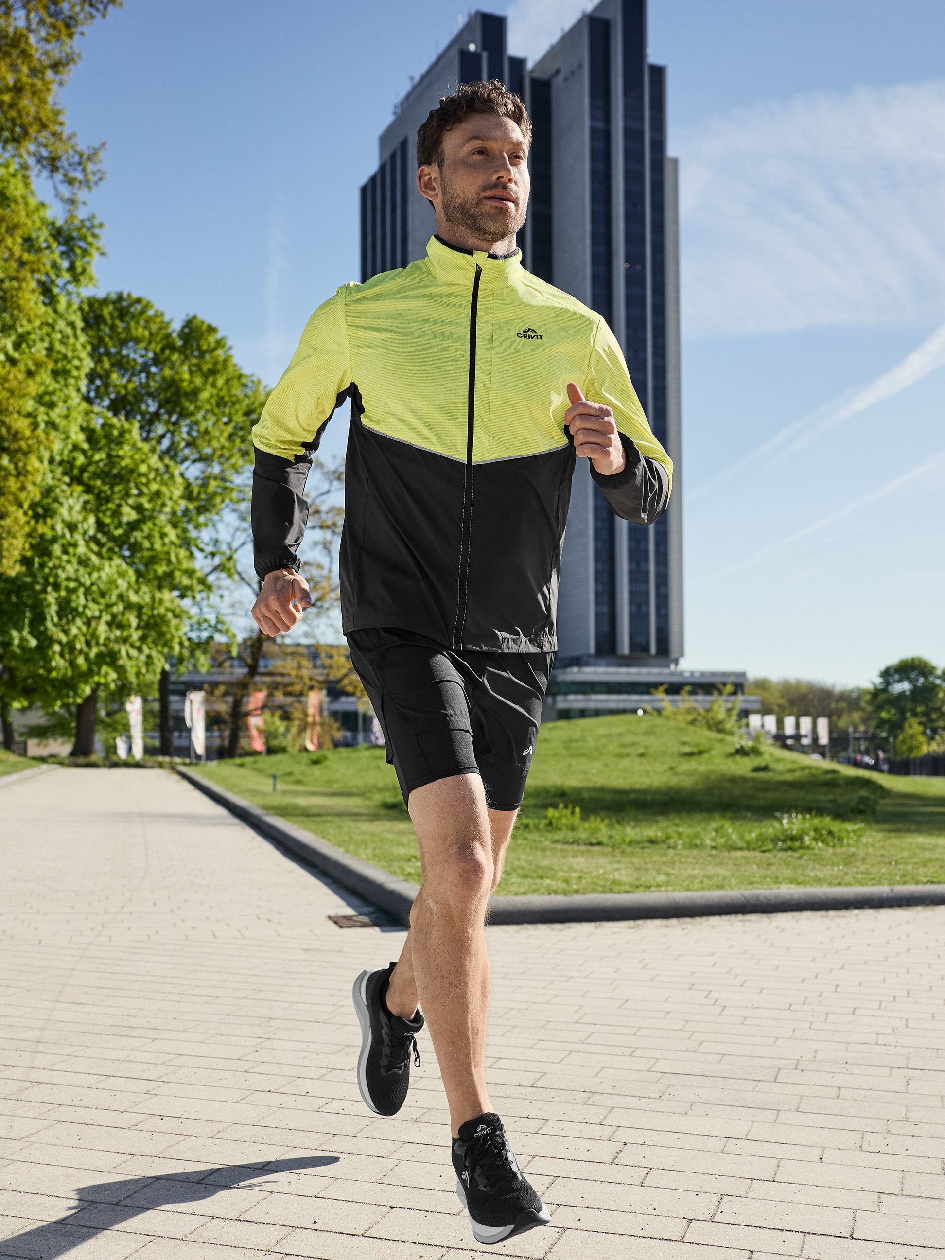 Mann in gelb-schwarzer Laufjacke und schwarzen Shorts, draußen laufend.
