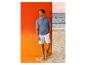 Mann im blauen Feinstrick-Poloshirt und weißen Shorts am Strand.