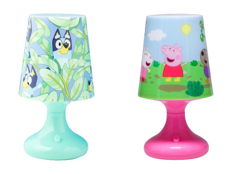 Zwei Kinder-Tischlampen: eine mit blauen Hundefiguren und grünen Blättern, die andere mit Schweinefiguren auf einem Feld.