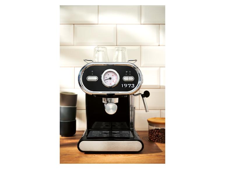 Schwarze Kaffeemaschine vor einer weißen Fliesenwand auf einer Holztheke