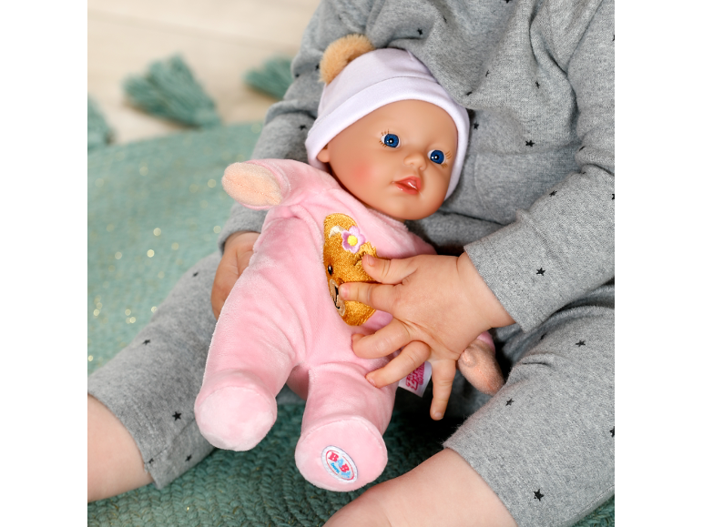 Ein Kind hält eine Baby-Puppe in einem rosa Strampler und einer weißen Mütze.
