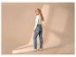 Blonde Frau in Jeans und weißem Langarmshirt, blickt über die Schulter.