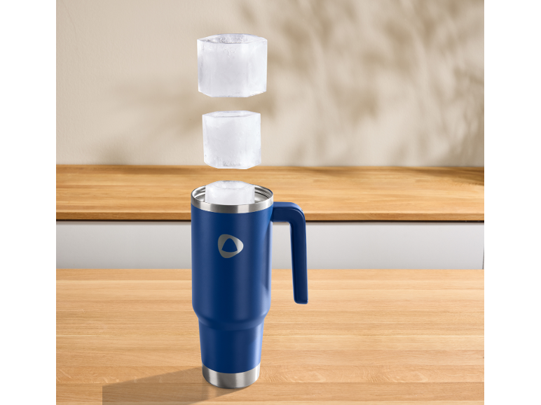 Blauer Isolierbecher mit Griff, mit Eiswürfeln darüber schwebend auf einer Holztheke.