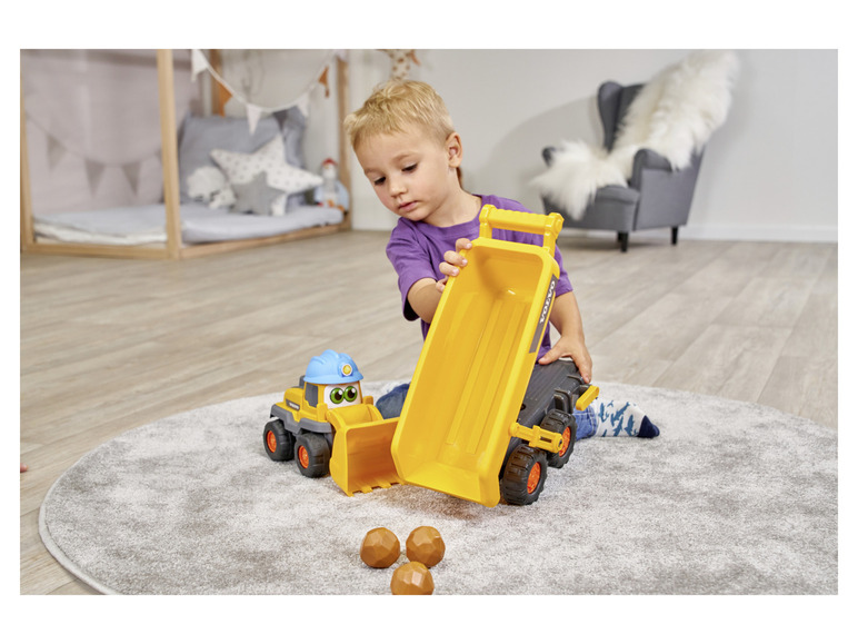 Ein Kind spielt mit einem gelben Volvo LKW und einem Bagger auf einem Teppich.