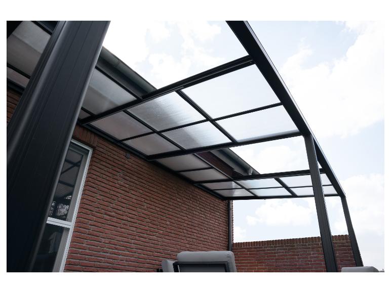 Terrassenüberdachung mit transparentem Dach und schwarzem Rahmen an einer Ziegelwand.