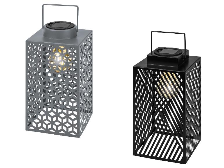 Zwei Solarleuchten in Grau und Schwarz mit ausgeschnittenen Mustern und leuchtenden Glühbirnen.