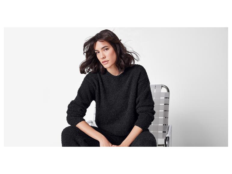 Eine Frau in einem schwarzen flauschigen Pullover und Hose sitzt auf einem Stuhl.