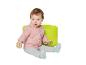 Baby in rosa Hoodie und grauer Hose, sitzt auf einem grünen Sitzsack mit Holzklotz.