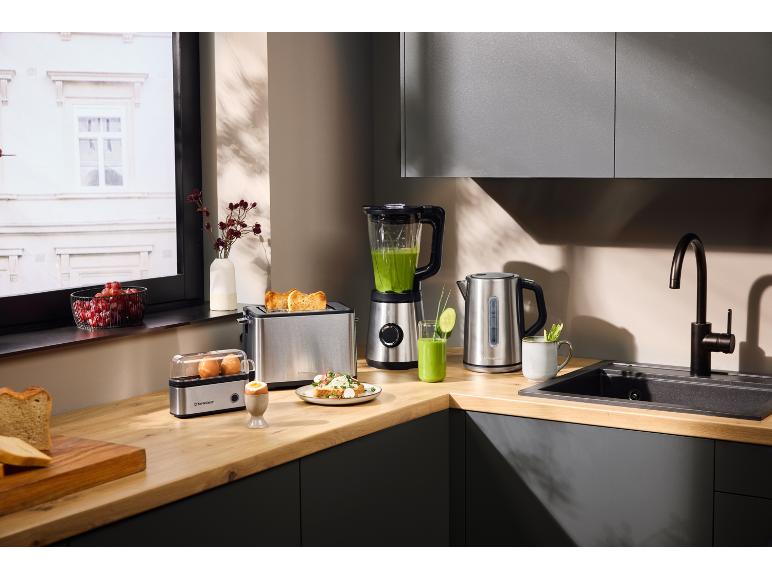 Küchen-Frühstücksset: Toaster, Mixer, Wasserkocher, Eierkocher und frische Speisen auf Holzarbeitsplatte.