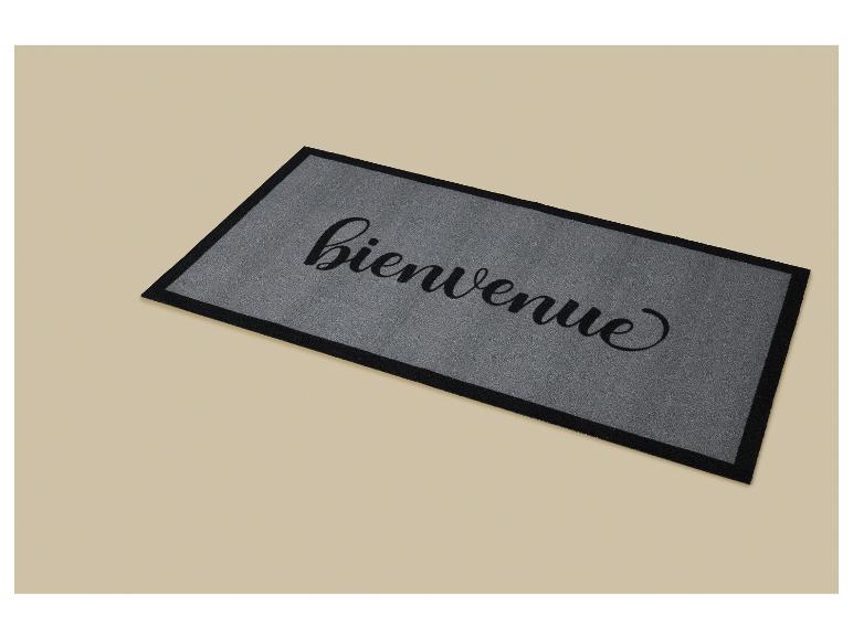 Graue Fußmatte mit dem Schriftzug „bienvenue“ (Willkommen) in schwarzer Kursivschrift.