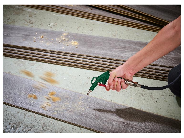 Eine Person benutzt eine Druckluftpistole, um Sägespäne von einer Laminatdiele zu entfernen.