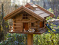 Ein hölzernes Vogelhaus im Chaletstil mit einem blauen Vogel darauf