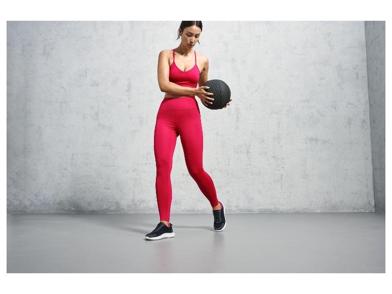 Eine Frau in pinker Sportkleidung mit einem schwarzen Medizinball.