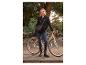 Frau in schwarzer Jacke und Jeans, steht neben einem Fahrrad mit Umhängetasche.