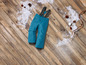 Blaue Skihose mit Hosenträgern auf einem Holzboden mit Schnee