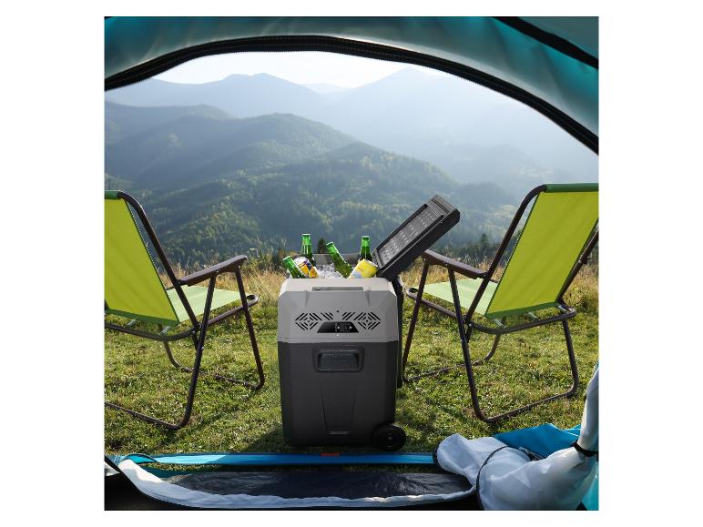 Tragbare Kühlbox mit Getränken und zwei Campingstühlen vor einer Berglandschaft.