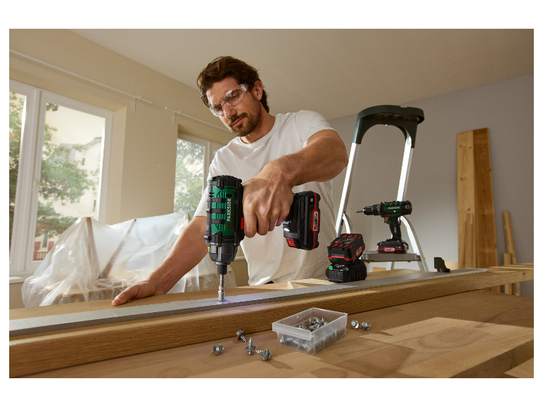 Ein Mann verwendet einen Parkside Schlagbohrschrauber, um in ein Stück Holz zu schrauben.