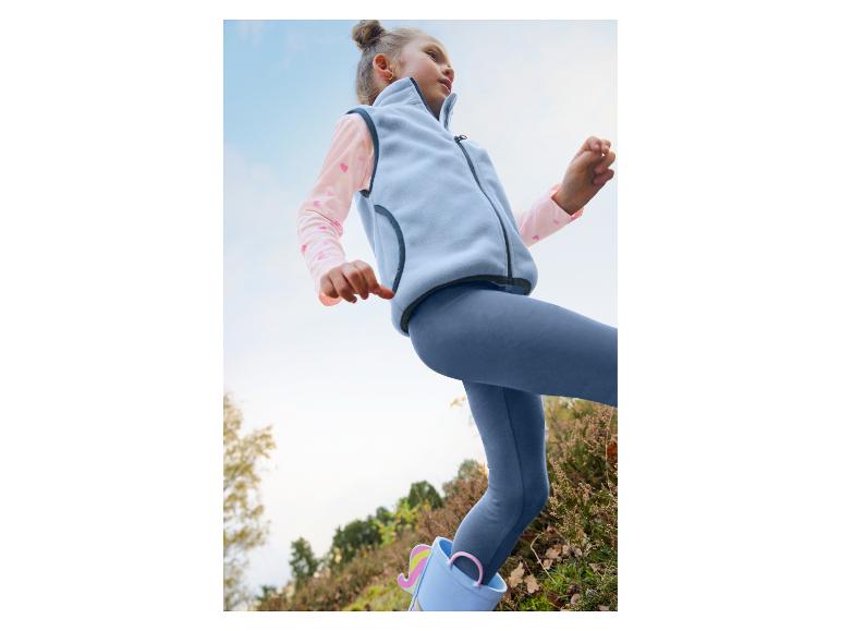 Mädchen in hellblauer Fleeceweste, rosa Langarmshirt, blauer Leggings und Einhorn-Gummistiefeln