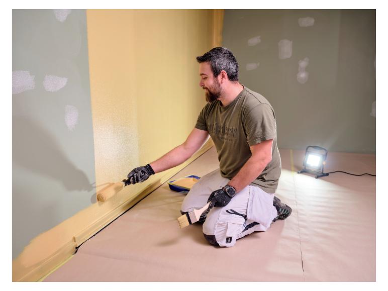 Mann streicht Wand, beleuchtet von LIVARNO® Arbeitsleuchte „The Painter+“.