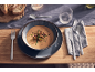 Eine Schüssel cremige Suppe serviert mit Besteck und Brot auf einem gedeckten Tisch.